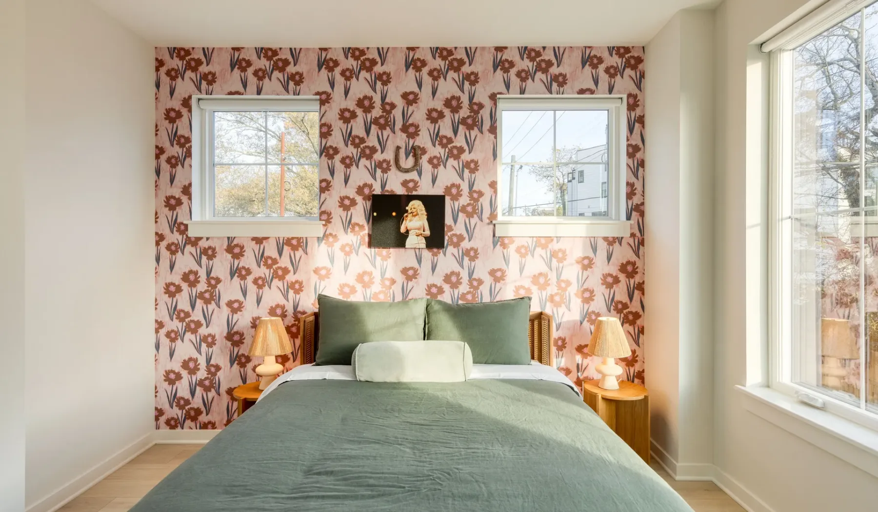 Un dormitorio con una cama frente a un papel pintado floral y ventanas a ambos lados.