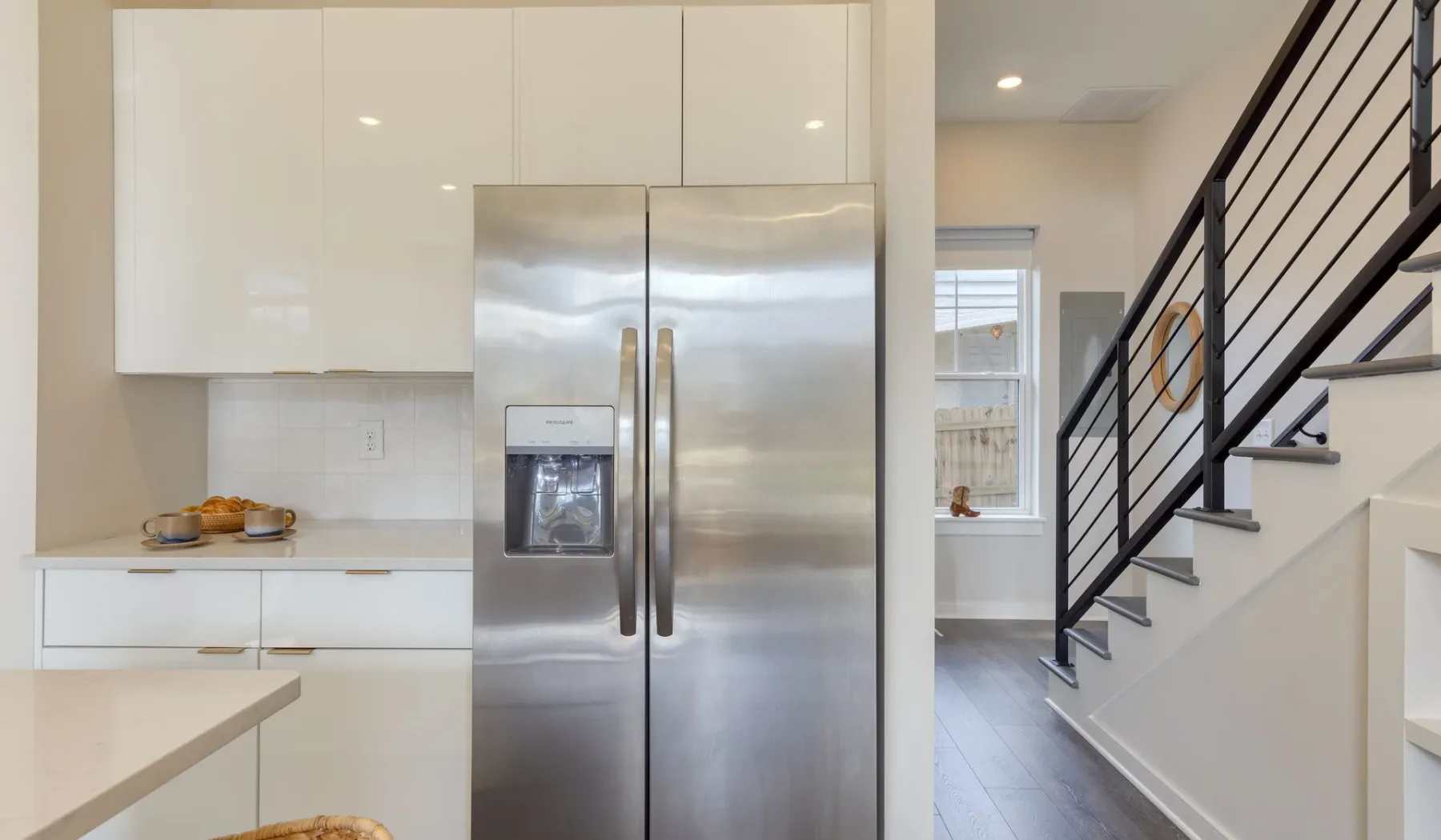 Una cocina luminosa con un refrigerador de acero inoxidable junto a una escalera.