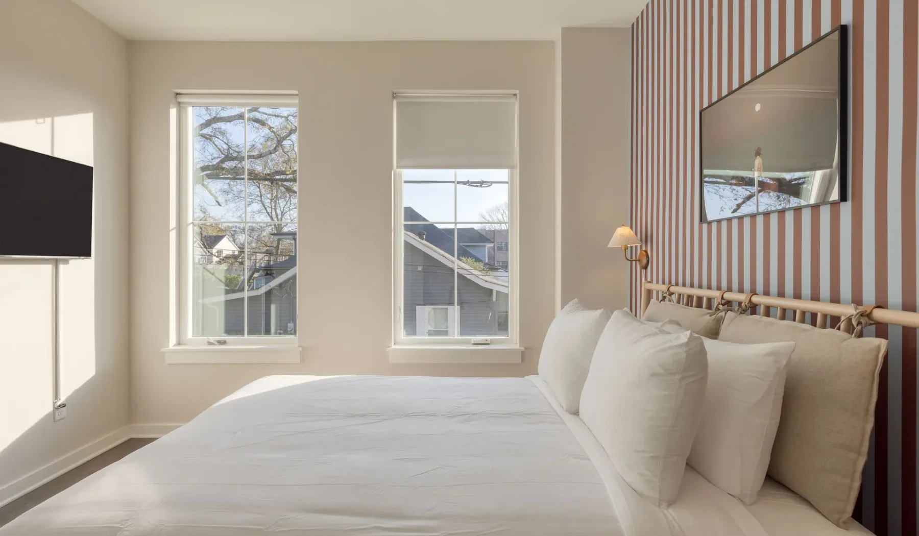 Un dormitorio luminoso con una cama, grandes ventanas y una pared decorativa a rayas.