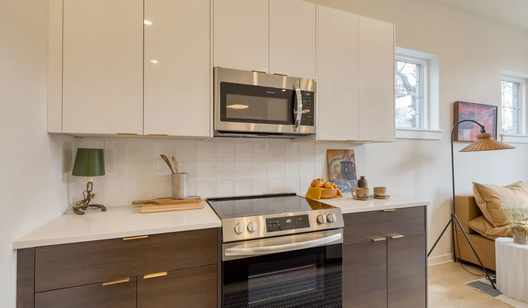 Una cocina luminosa con gabinetes blancos, muebles inferiores oscuros y una estufa de acero inoxidable.