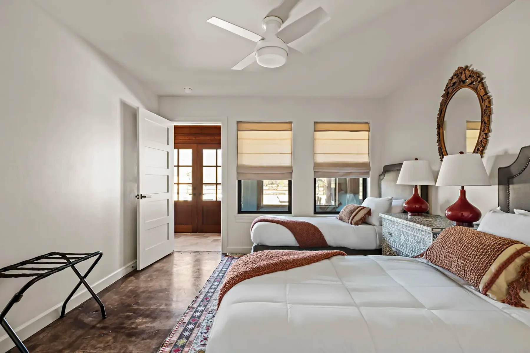 Dormitorio con dos camas, un ventilador de techo y ventanas con persianas de color claro.