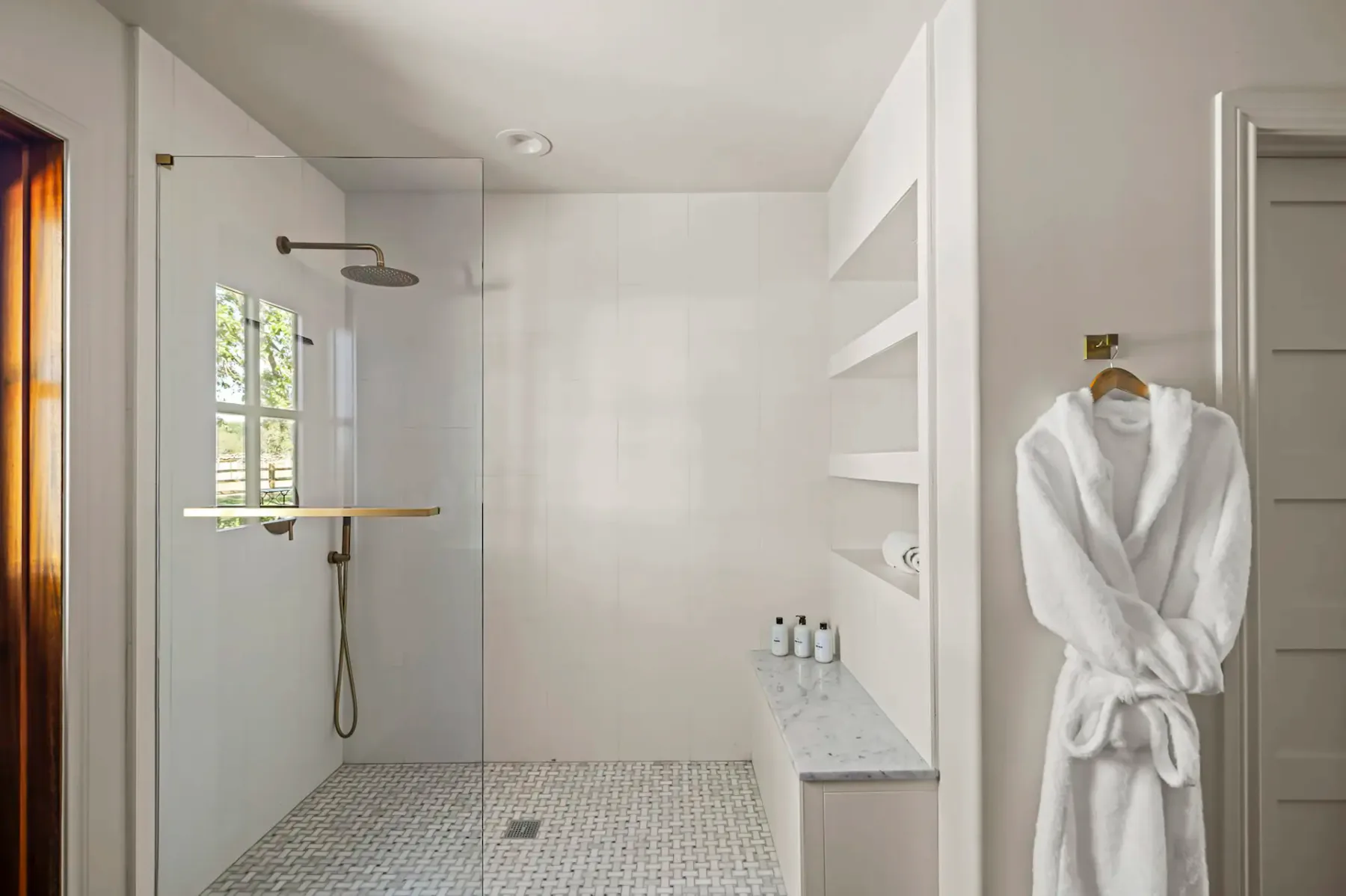 Un baño luminoso con ducha de vidrio y una bata blanca colgada en la pared.