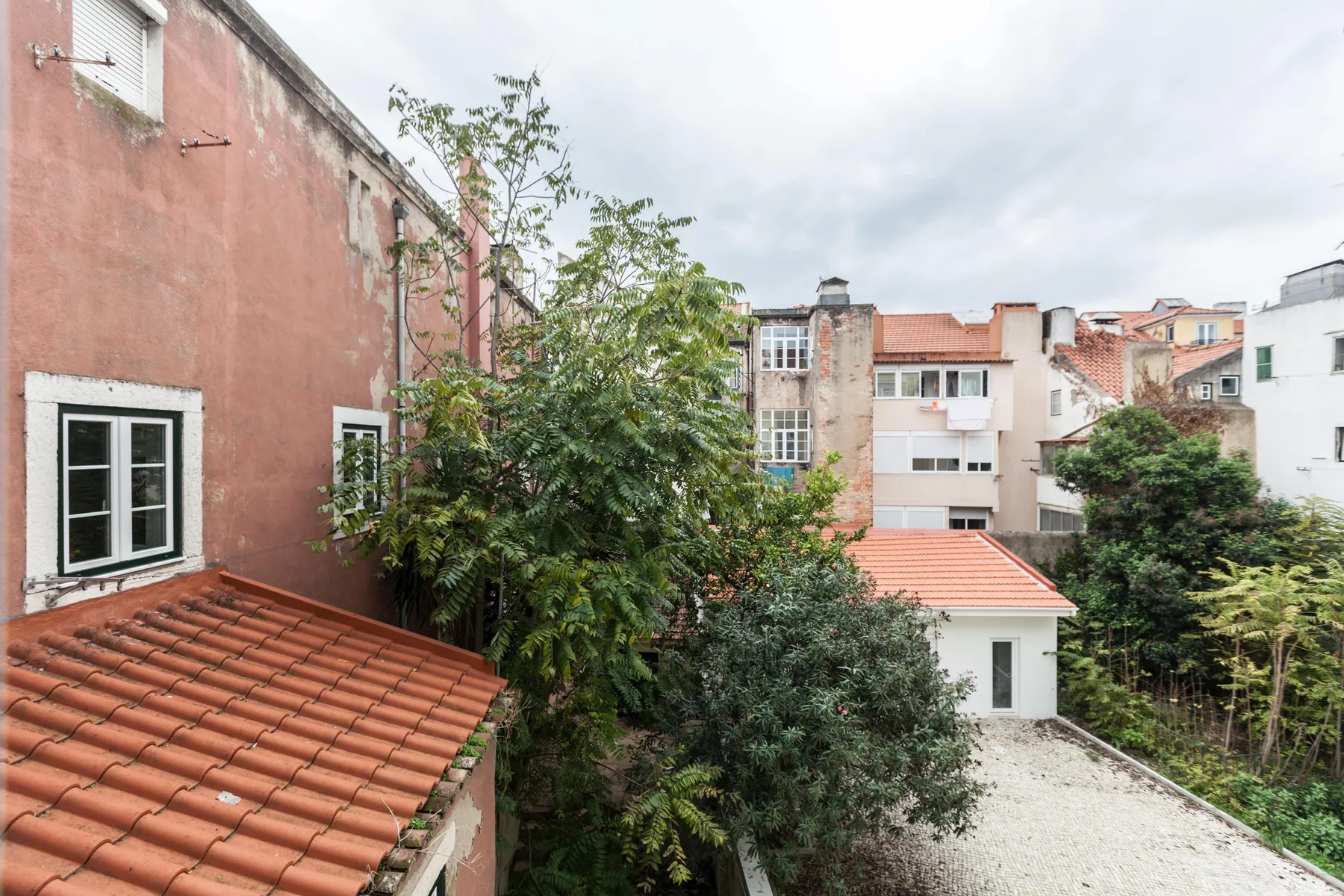 Un patio frondoso está rodeado de edificios de apartamentos y tejados de tejas rojas.