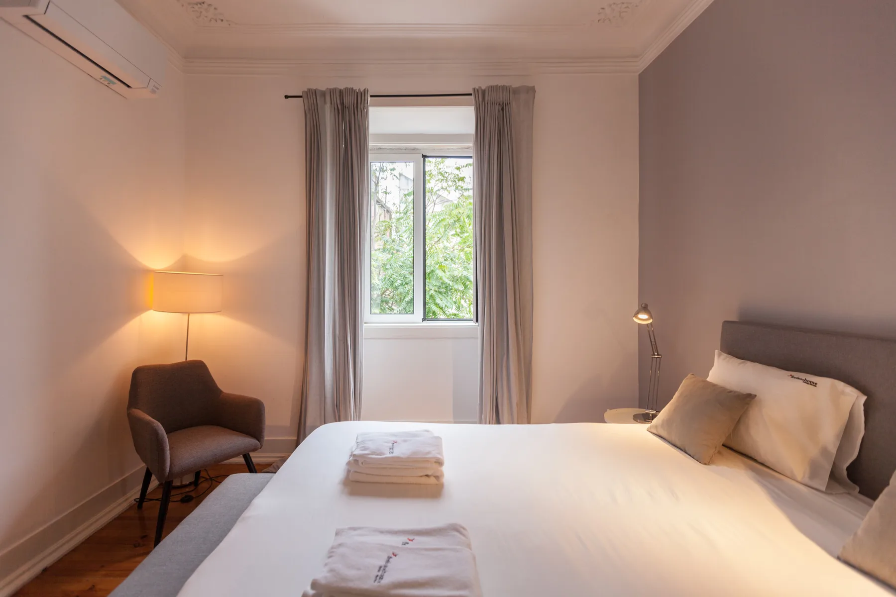 Un dormitorio con una cama, una ventana y cortinas grises.