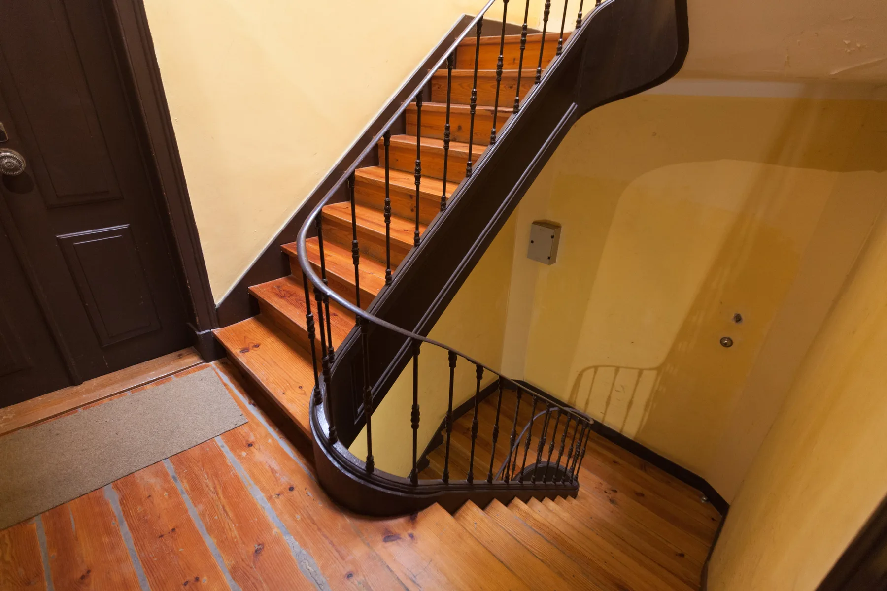Una escalera de madera con barandillas oscuras desciende por un interior de tonos cálidos.
