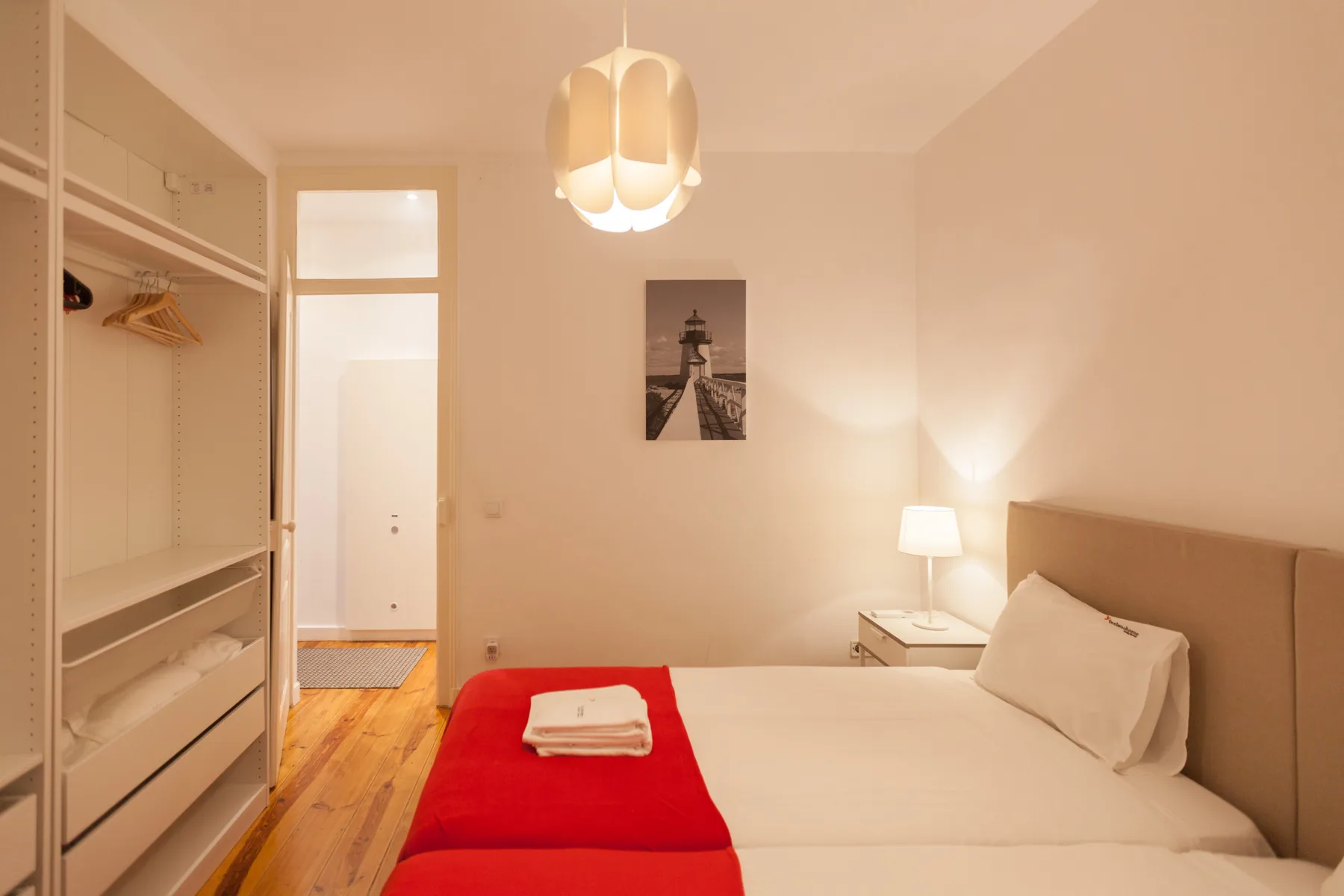 Dormitorio con cama, camino de cama rojo y armario abierto.