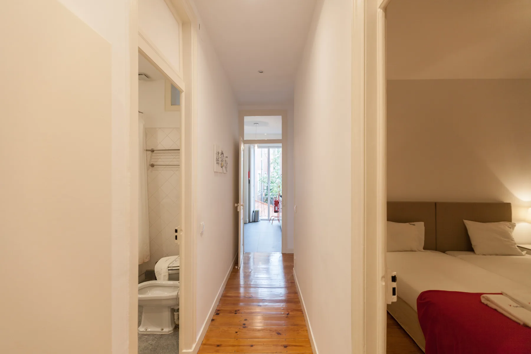 Un pasillo luminoso de apartamento con suelo de madera y puertas abiertas.