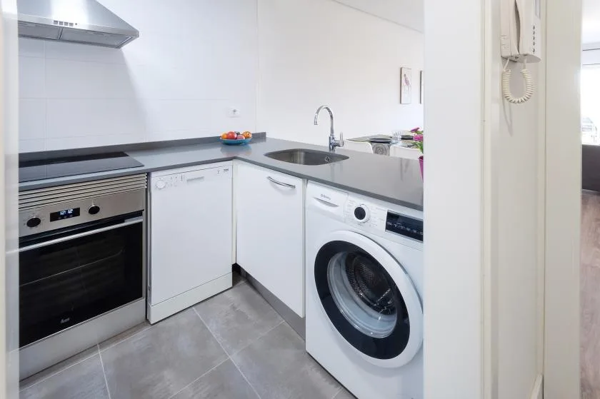 A compact kitchen with an oven, sink, and front-loading washing machine.