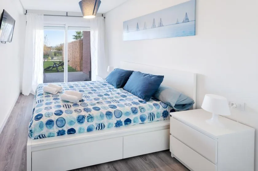 A bright bedroom with a bed covered in blue patterned bedding beside a white dresser.