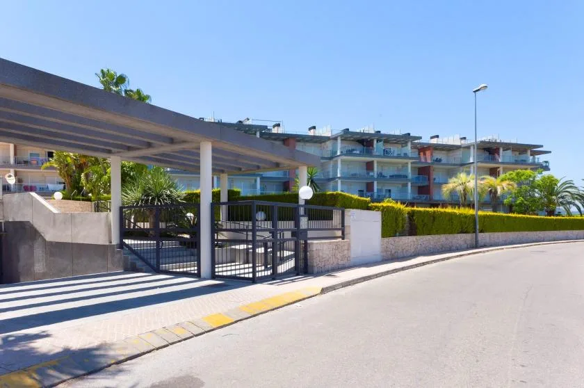 A modern apartment building stands behind a gated entrance and landscaped grounds.