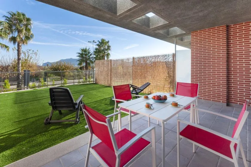 A covered outdoor patio with red seating and a dining table overlooks a lawn.