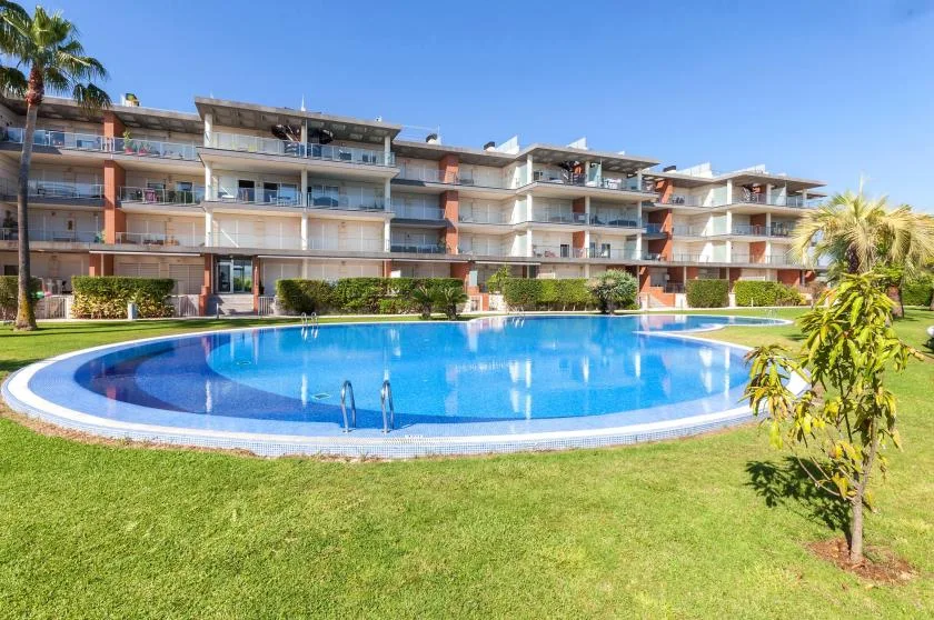 Una piscina curva ocupa un patio con césped frente a un edificio de varias plantas.
