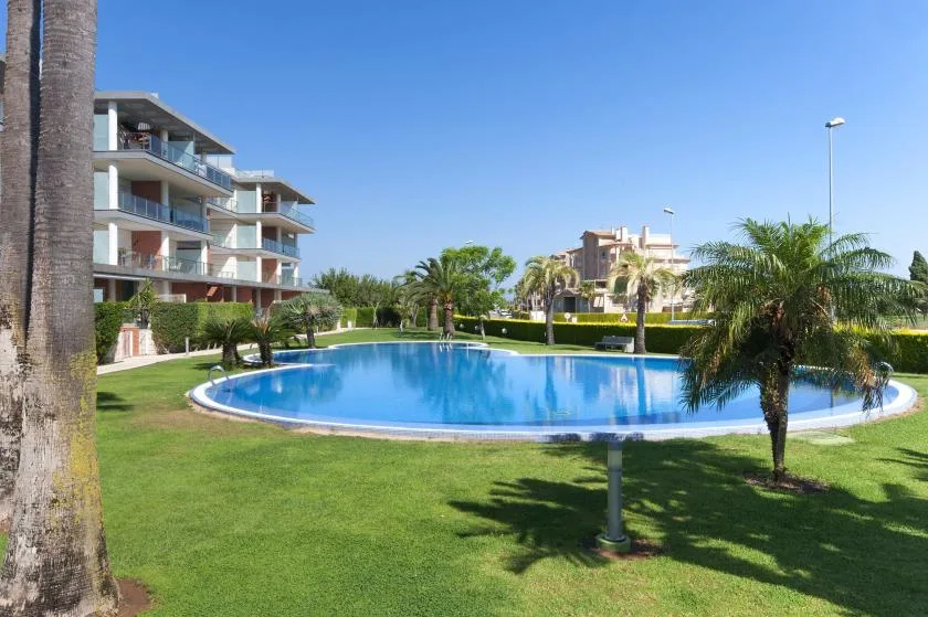 Una piscina curva está rodeada de césped y palmeras junto a edificios de apartamentos.