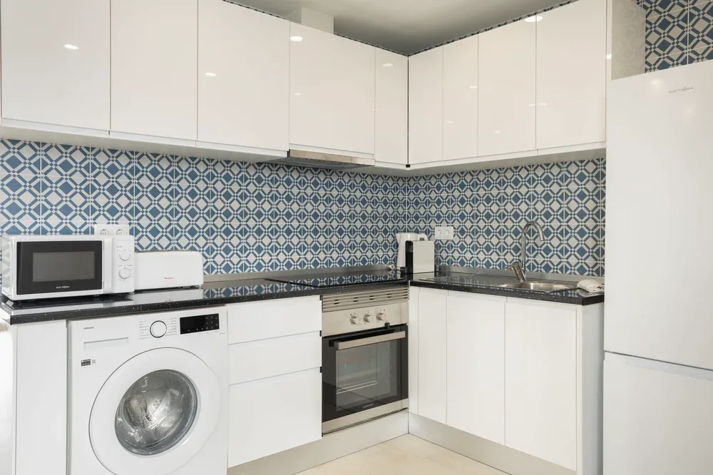 A modern kitchen with white cabinets, patterned backsplash, and built-in appliances.