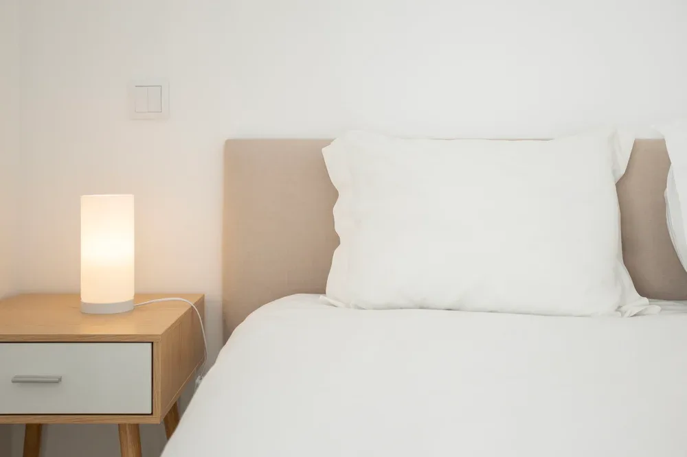 A bedroom with white bedding and a lit bedside lamp.