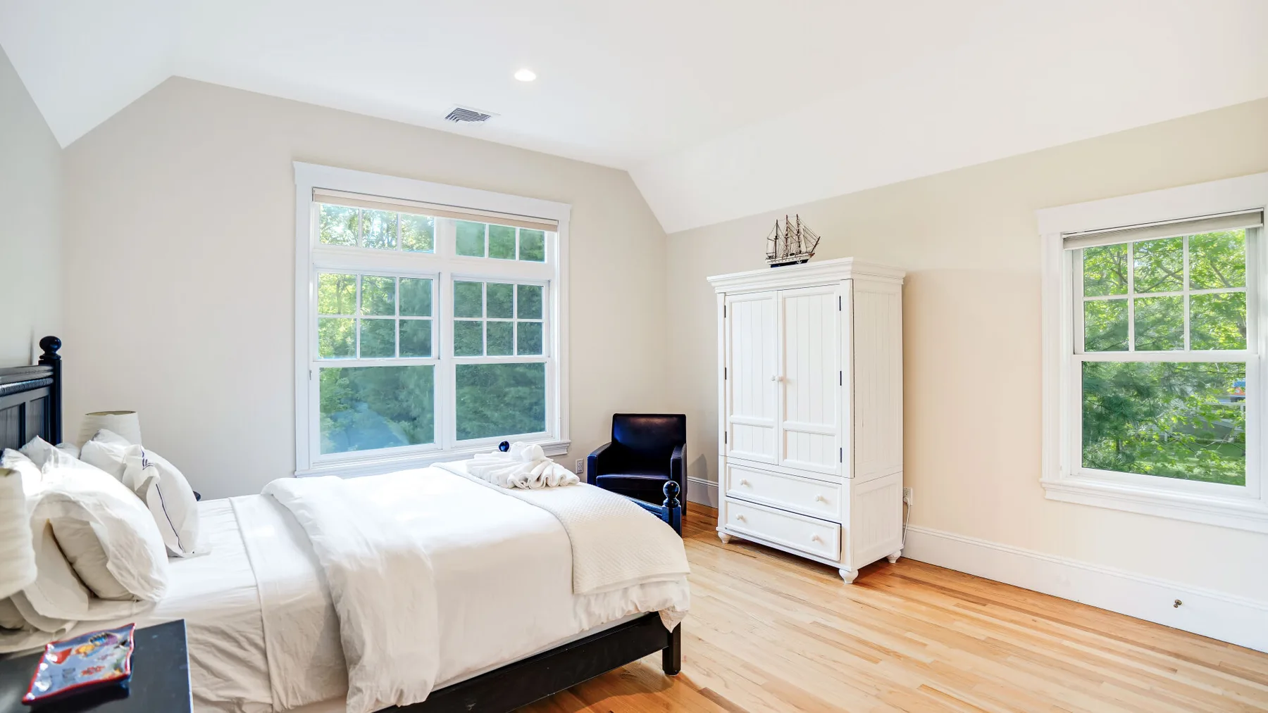 Un dormitorio luminoso con una cama, un armario blanco y ventanas con vistas a la vegetación.