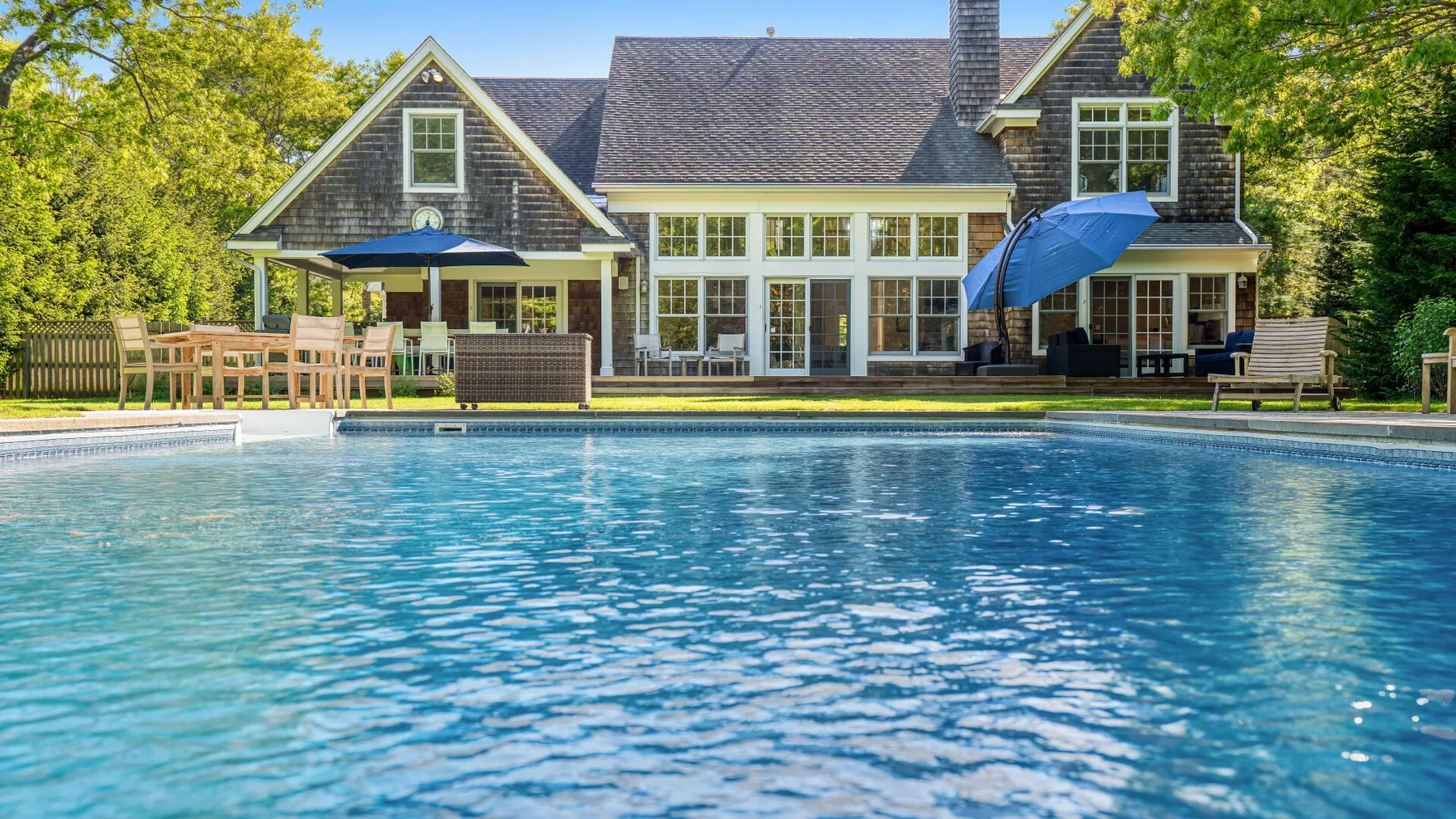 Una piscina frente a una casa grande rodeada de árboles.