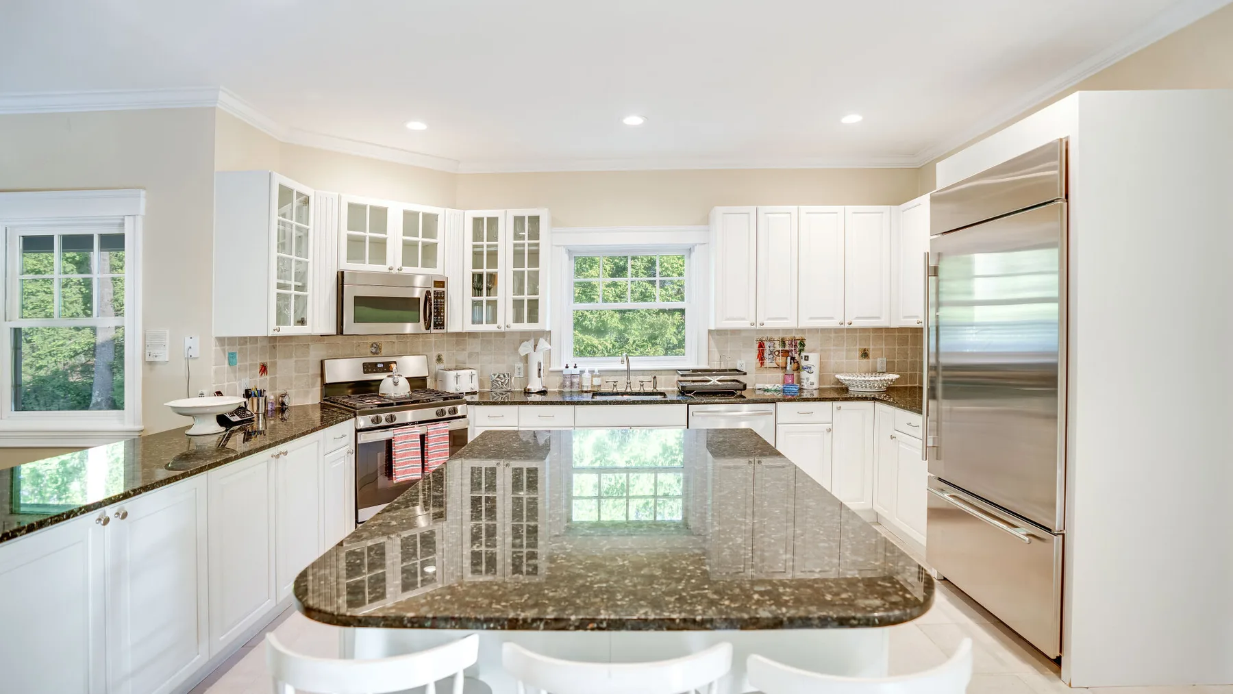 Una cocina luminosa con gabinetes blancos, electrodomésticos de acero inoxidable y una gran isla central.