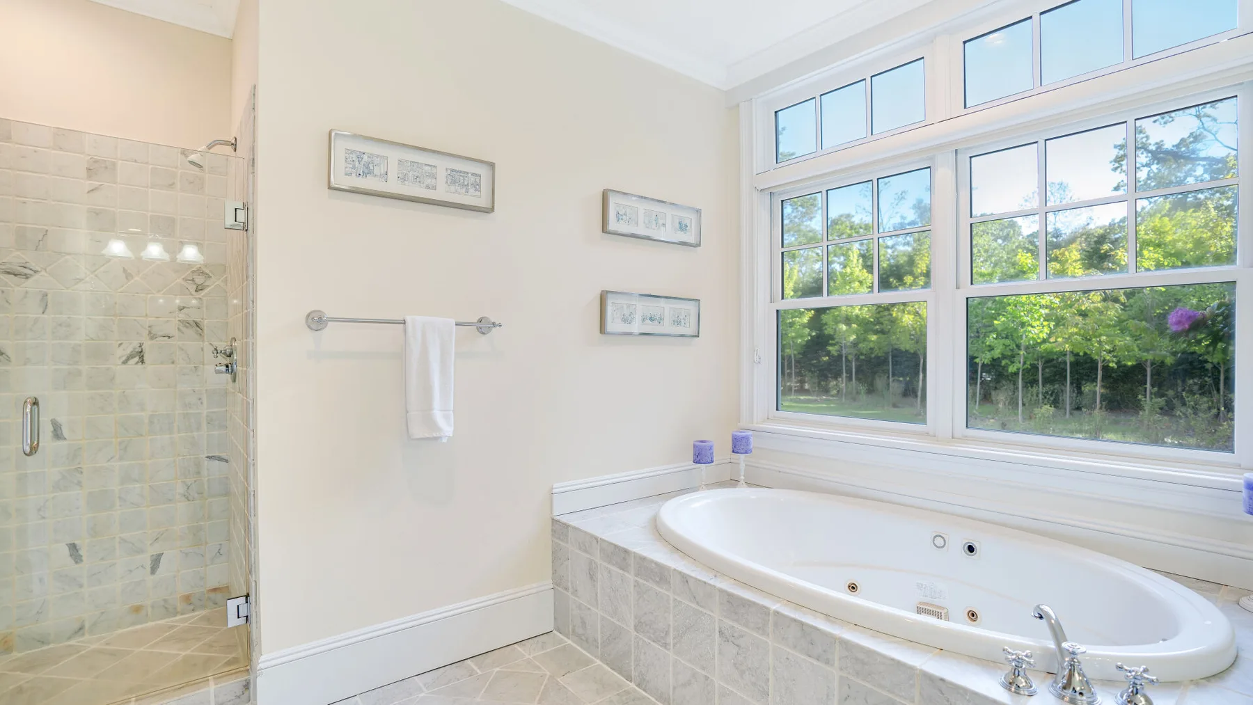 Un baño luminoso tiene una bañera bajo grandes ventanas.