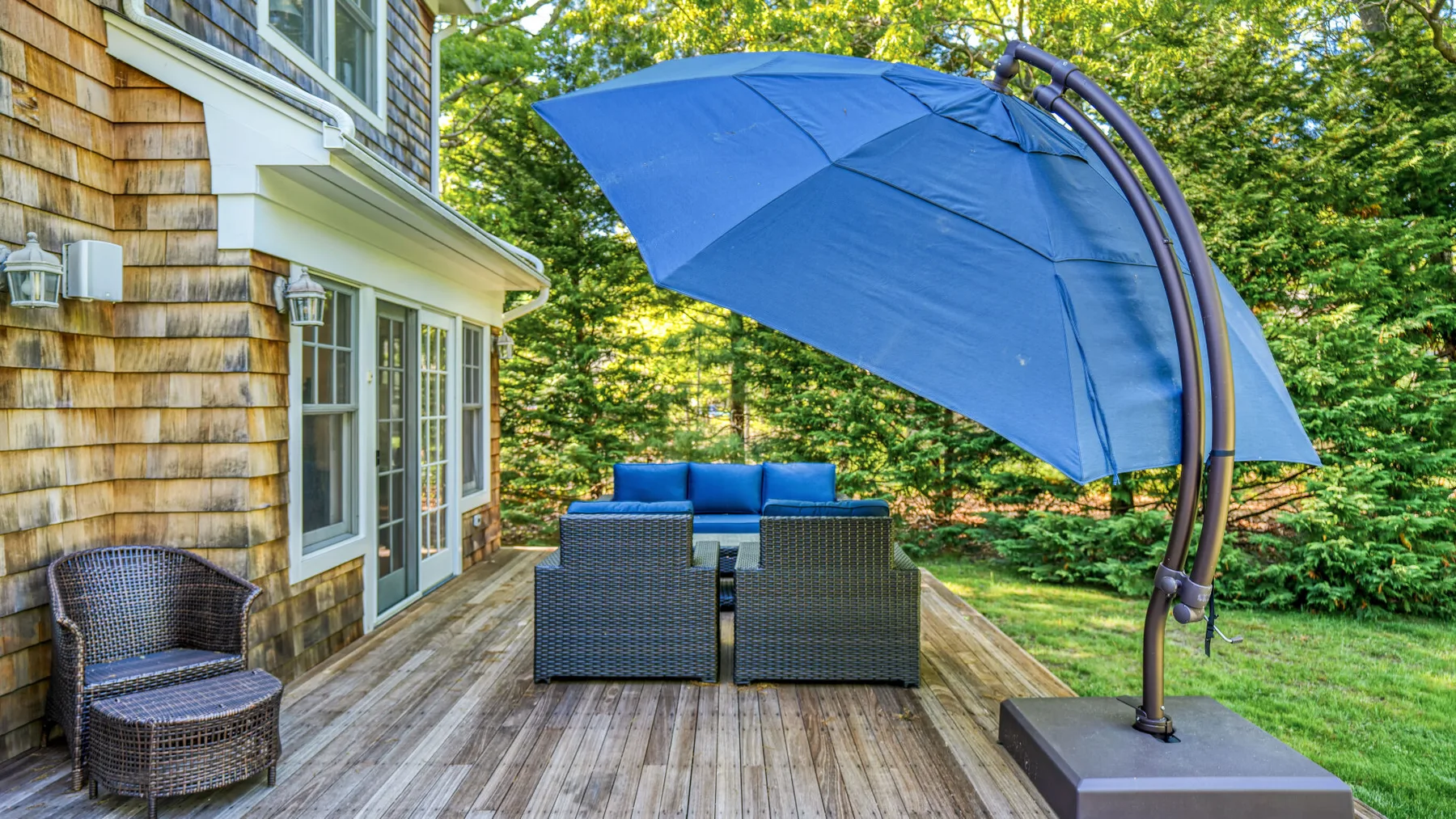 Una terraza exterior tiene asientos acolchados bajo una gran sombrilla azul.