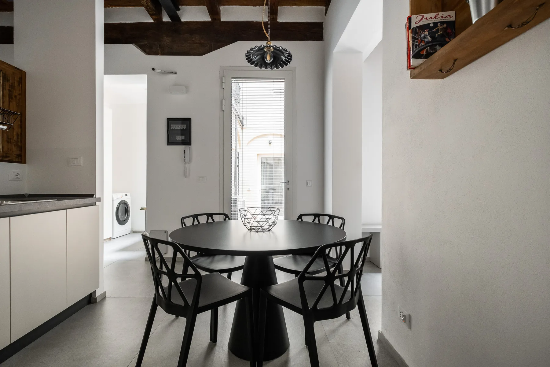 Comedor con una mesa redonda y sillas negras bajo vigas expuestas.