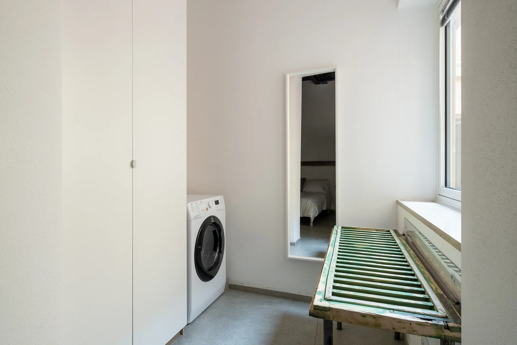A bright laundry room with a washing machine beside a long work surface.