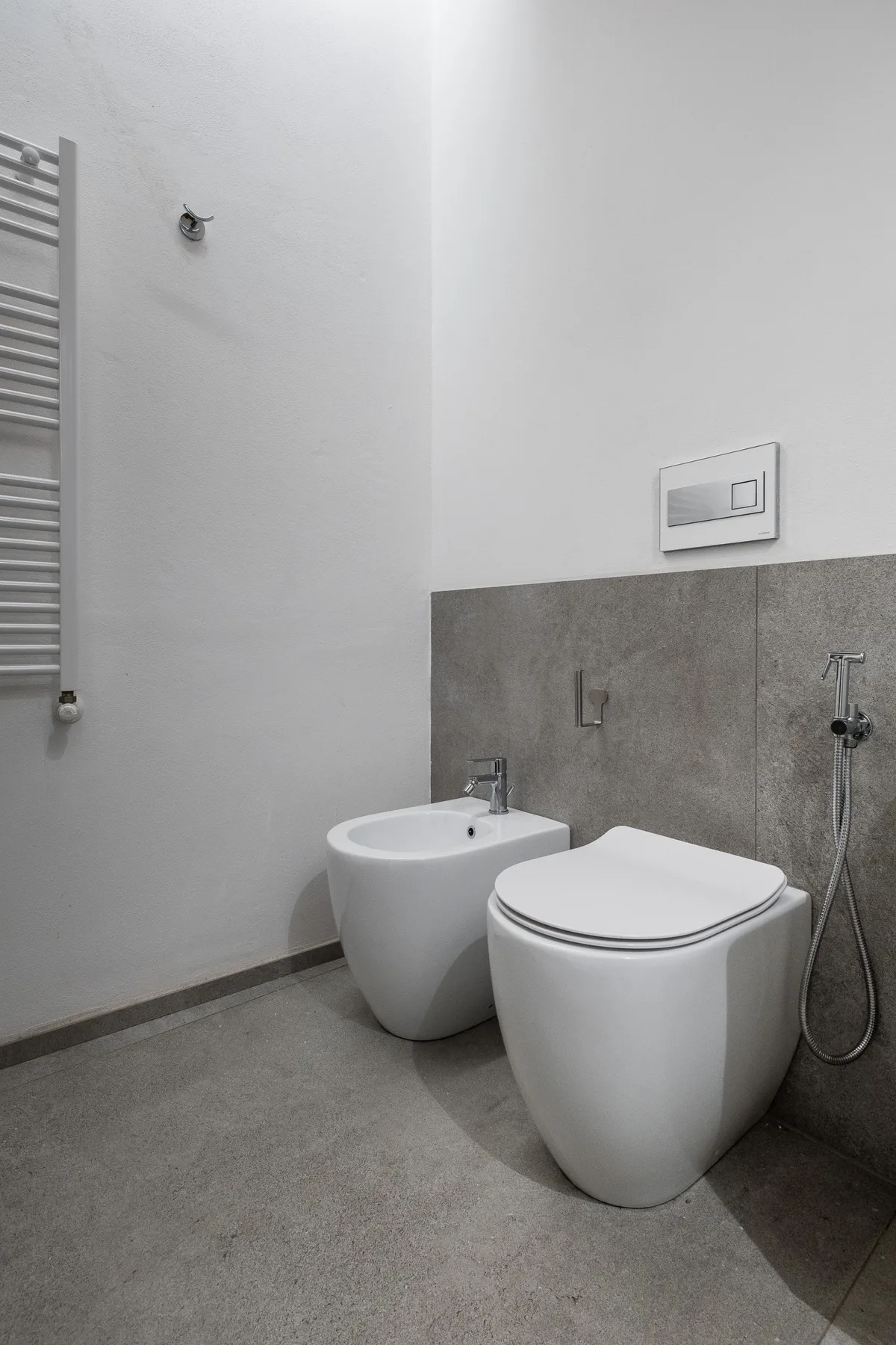 A modern bathroom with a toilet, bidet, and wall-mounted hand shower.