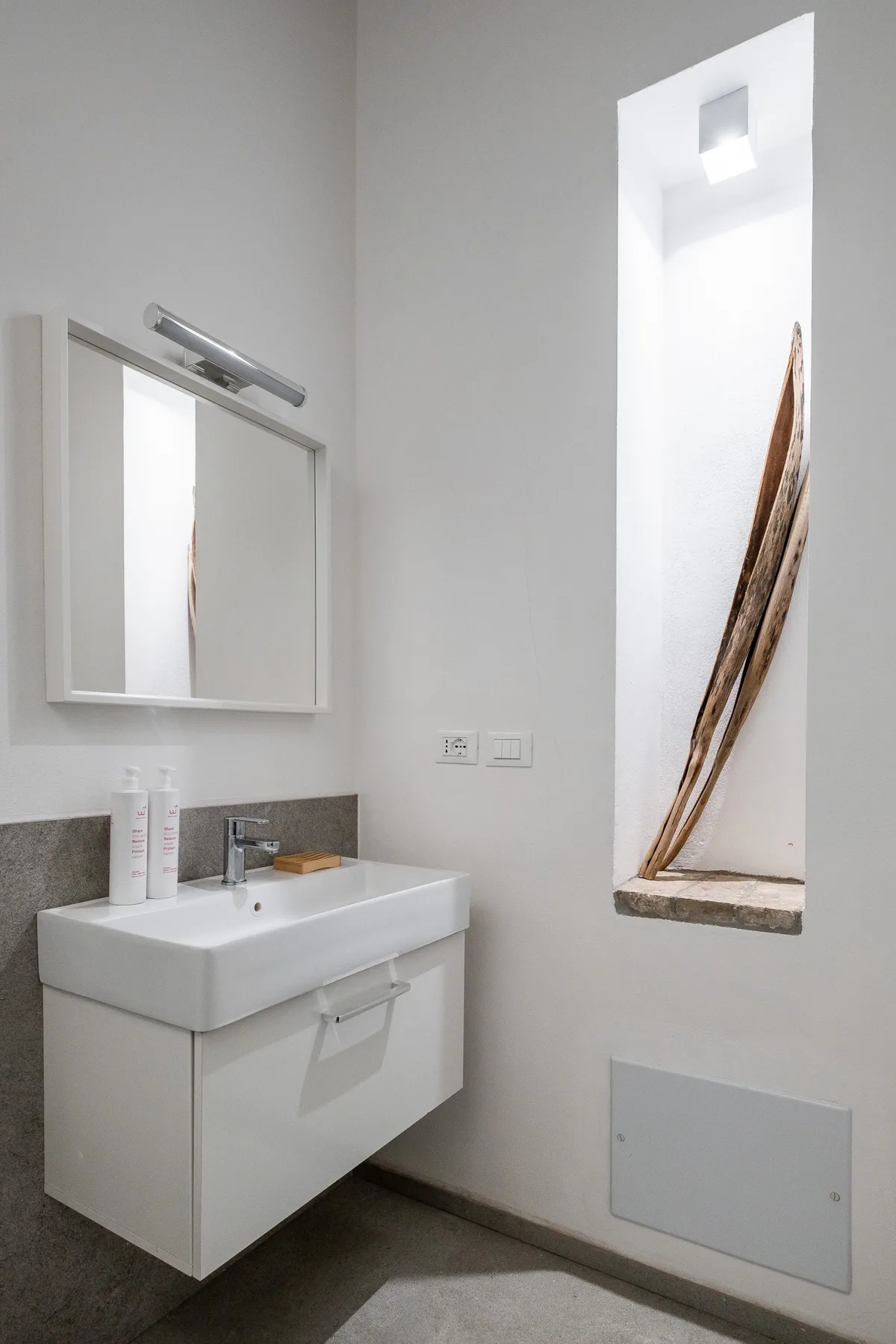A bathroom vanity with a wall mirror and a narrow recessed window.