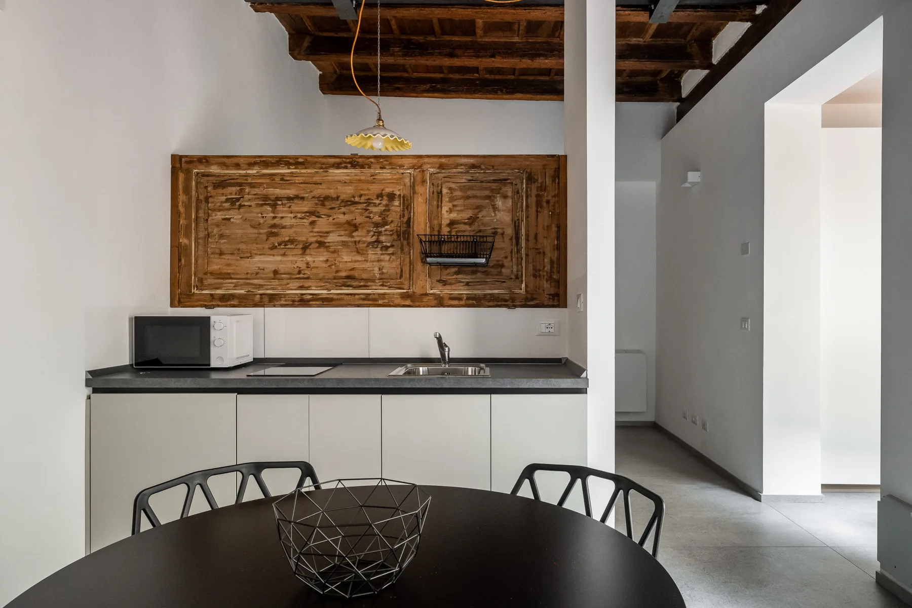 A modern kitchen and dining area with a dark round table beneath exposed wooden ceiling beams.