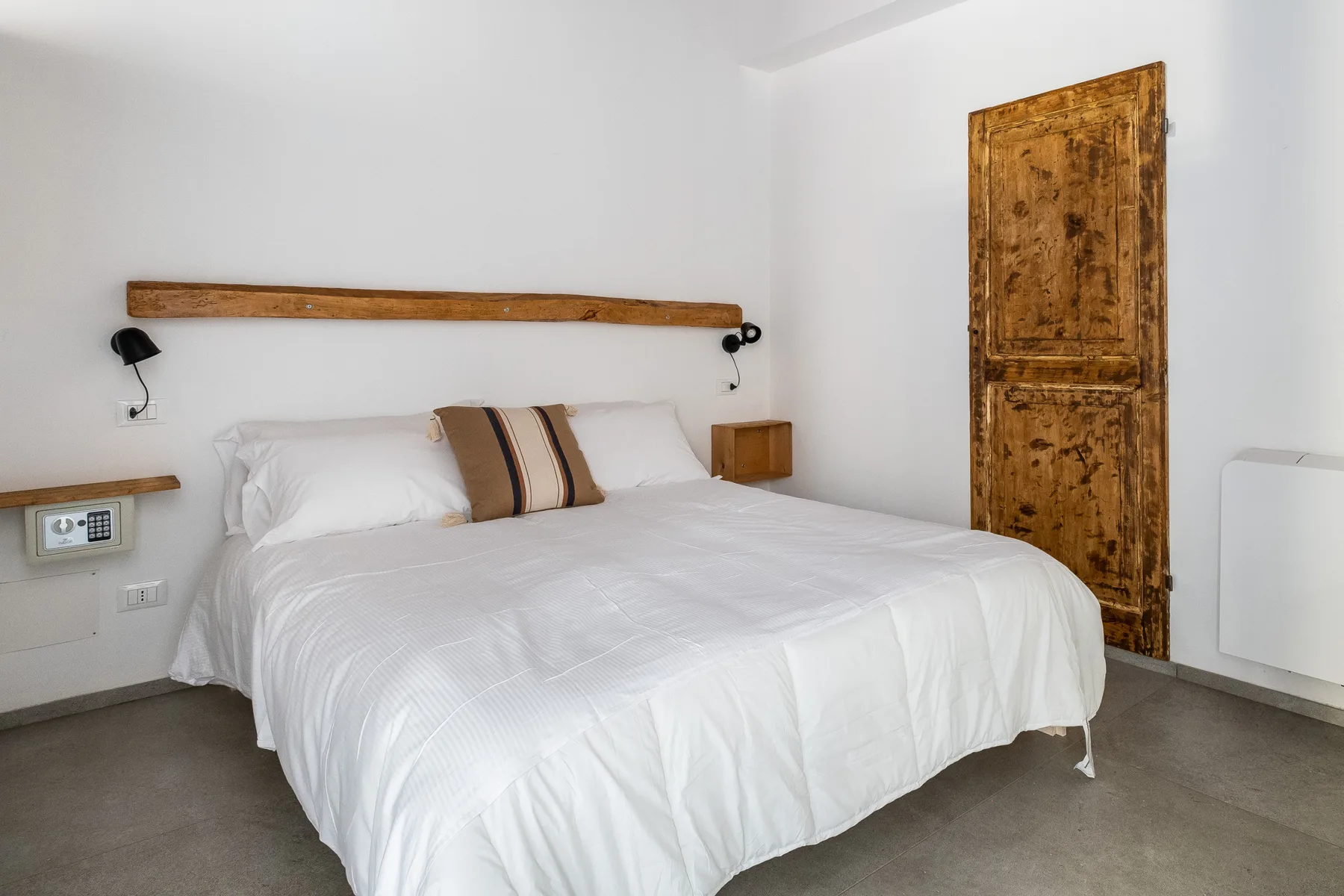 A bedroom with a bed dressed in white linens and a wooden door.