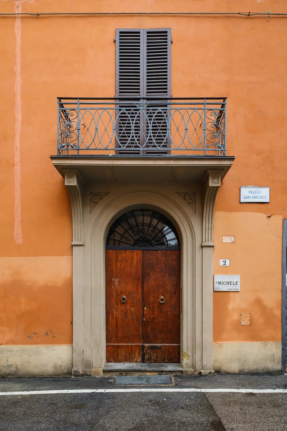 An ornate wooden entrance door beneath a balcony on an orange building.