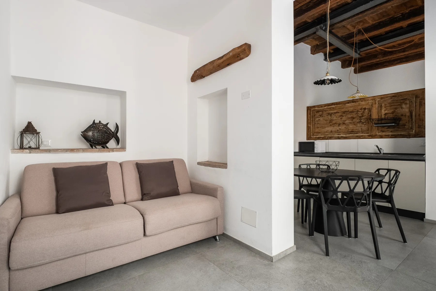 A living and dining area with a sofa and a dining table beneath exposed ceiling beams.