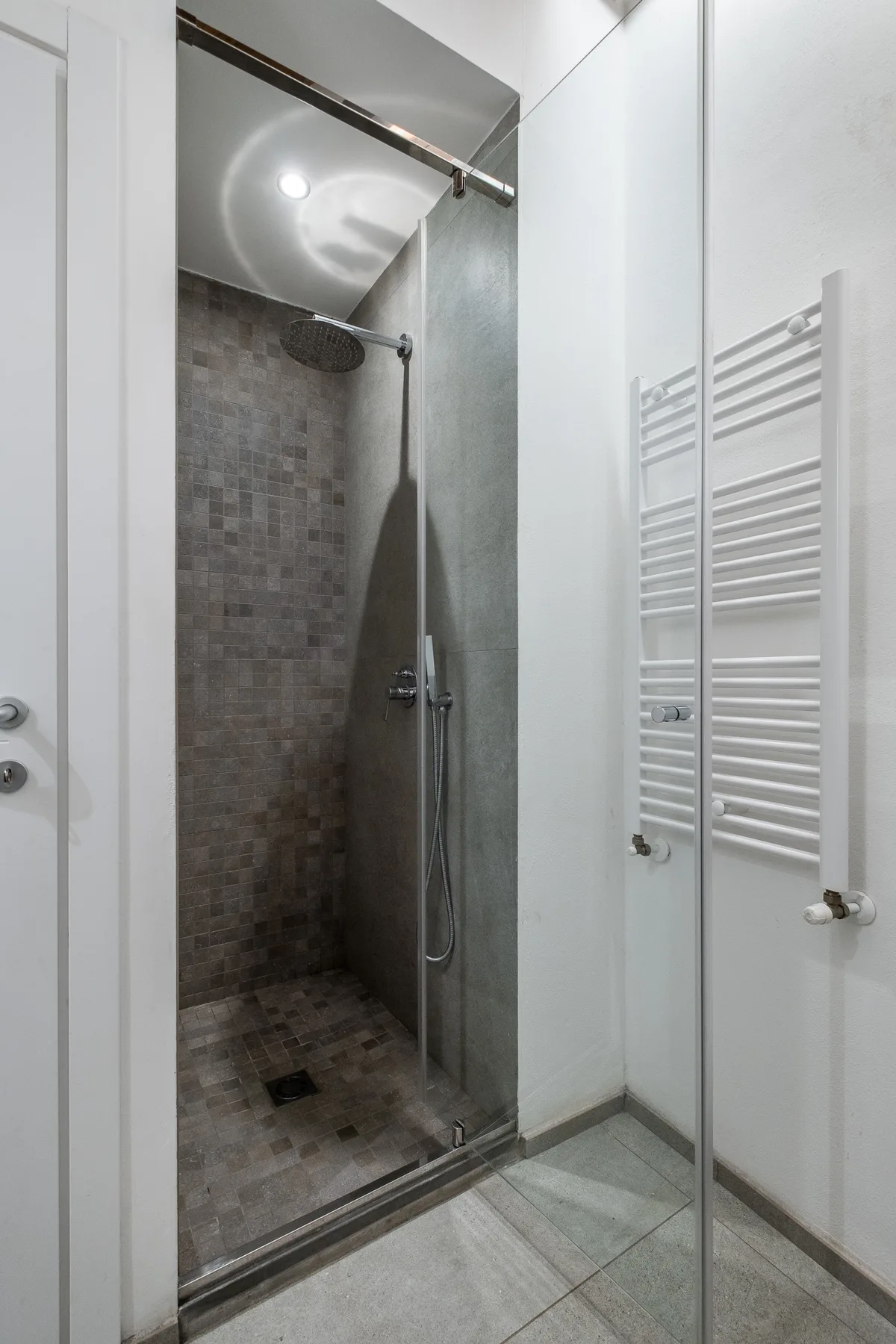 A tiled shower area with a glass panel and a wall-mounted towel warmer.