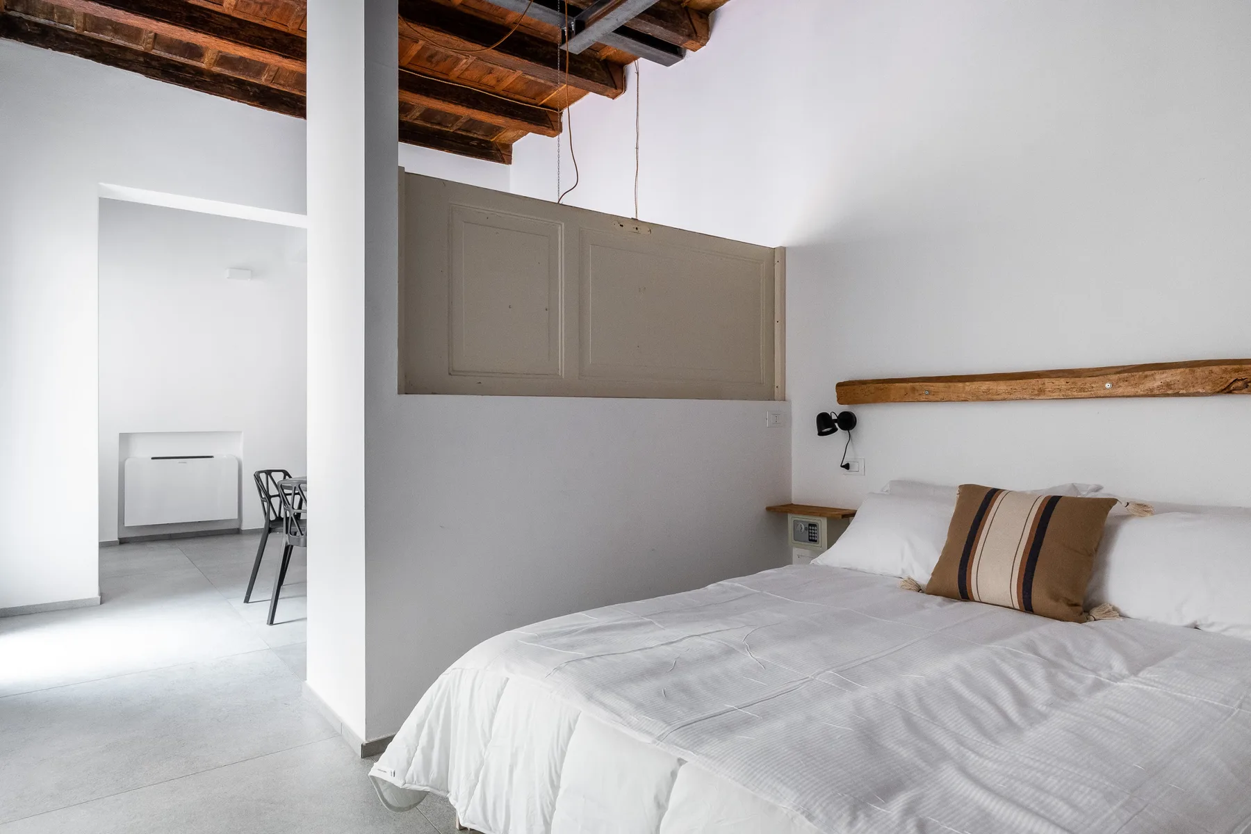 Un dormitorio luminoso con ropa de cama blanca y vigas de madera a la vista.