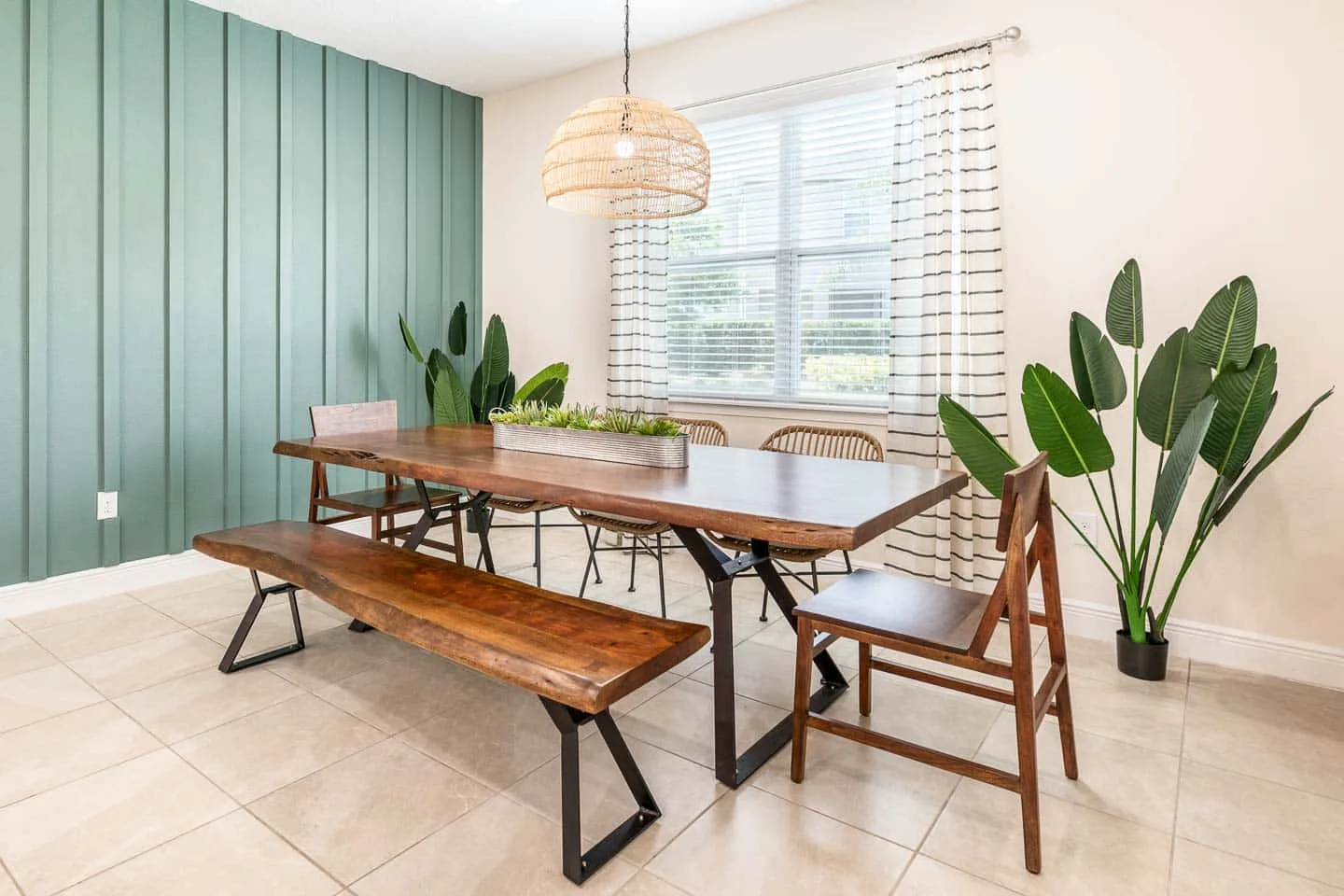 Un comedor tiene una mesa larga de madera, un banco y sillas junto a una ventana grande.