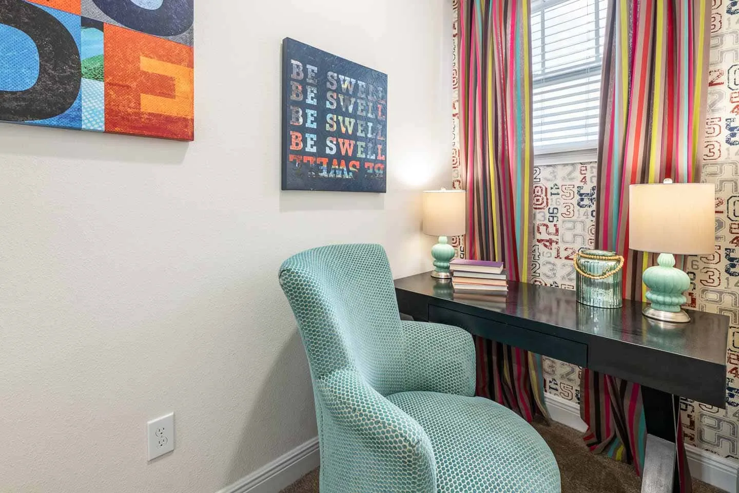 Un escritorio y un asiento tapizado están junto a una ventana con cortinas coloridas.