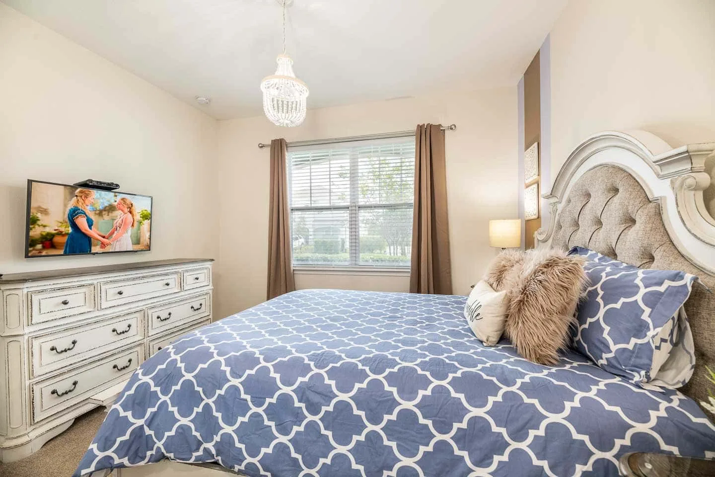 Un dormitorio con una colcha azul estampada, una cómoda y una ventana con cortinas.
