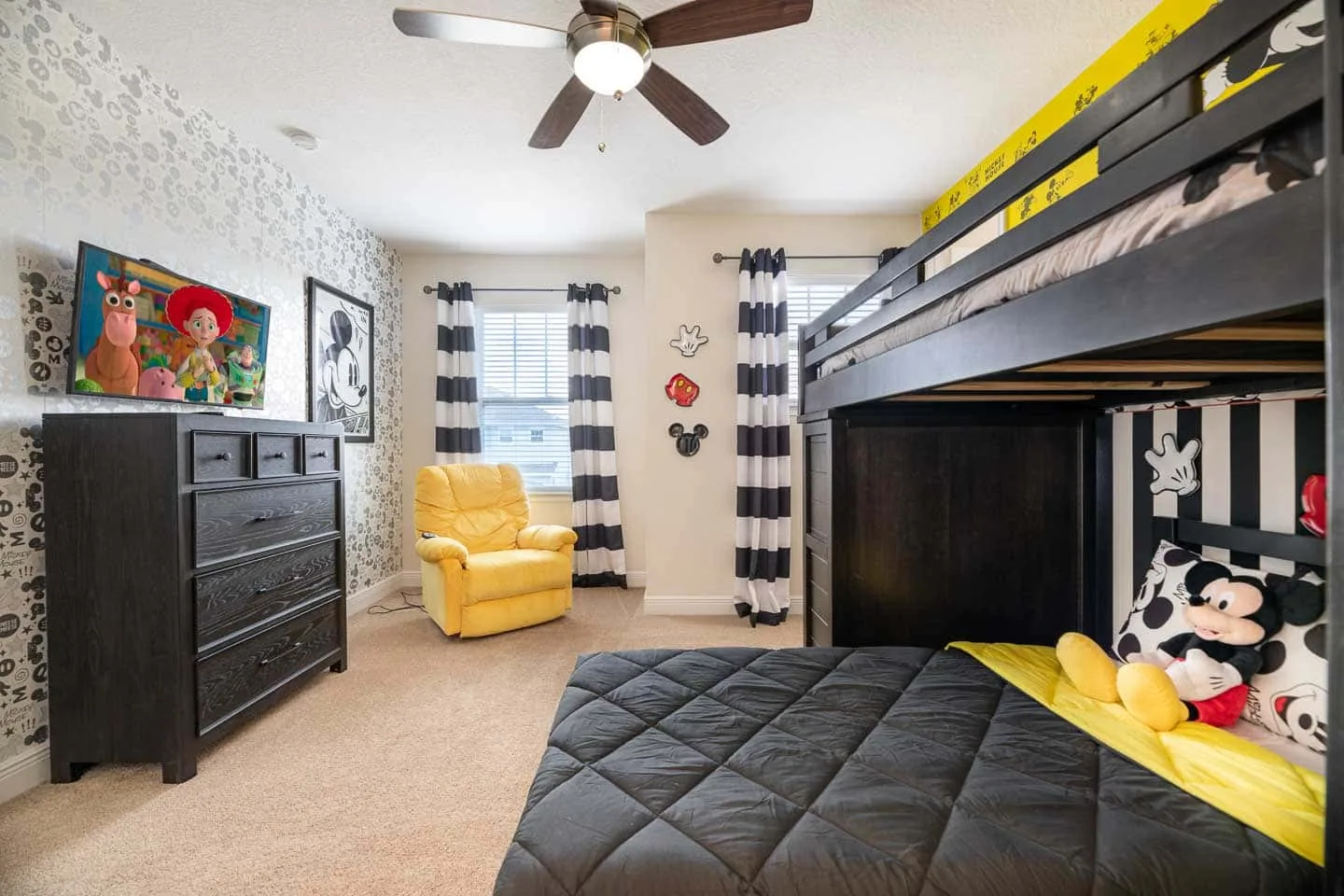 Un dormitorio con una cama elevada, un sillón amarillo y cortinas a rayas.