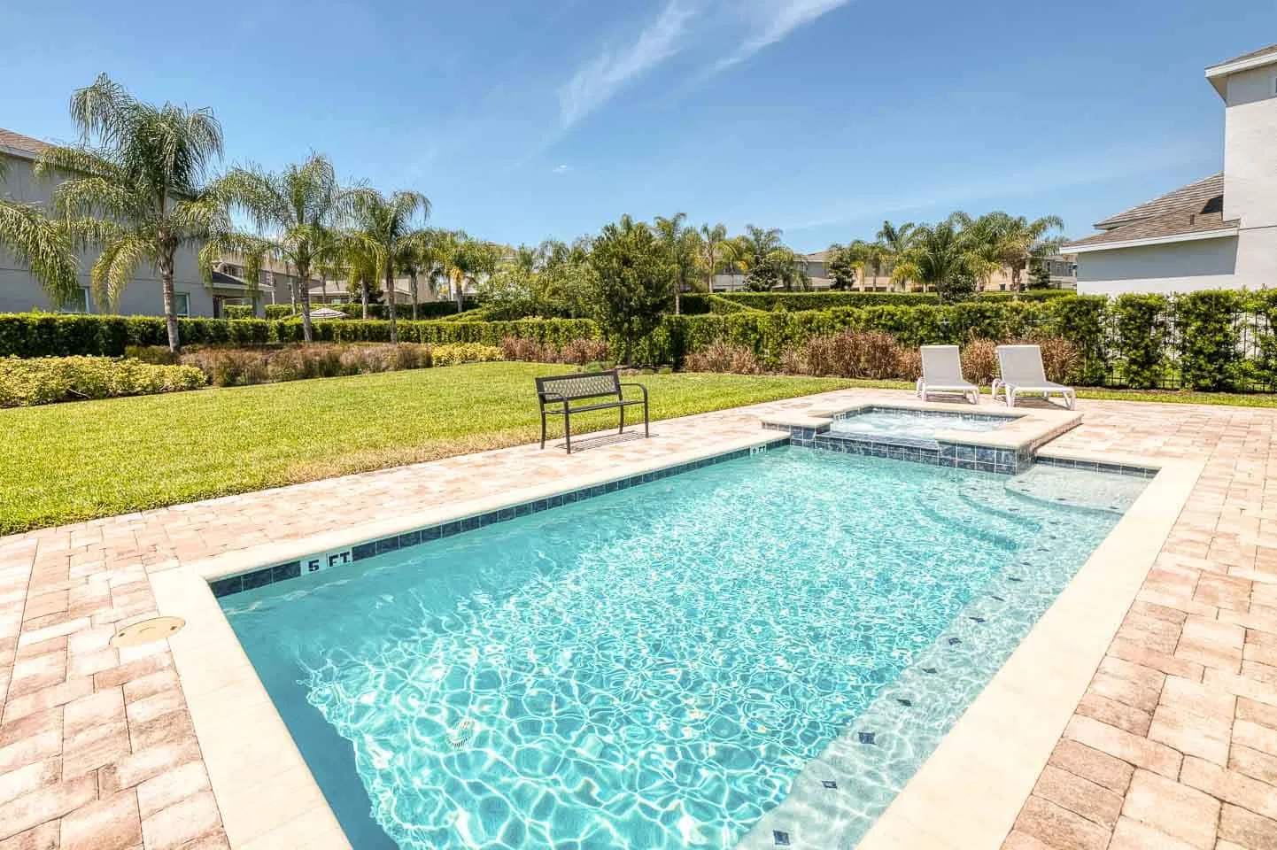 Una piscina al aire libre con un spa elevado y una terraza pavimentada.