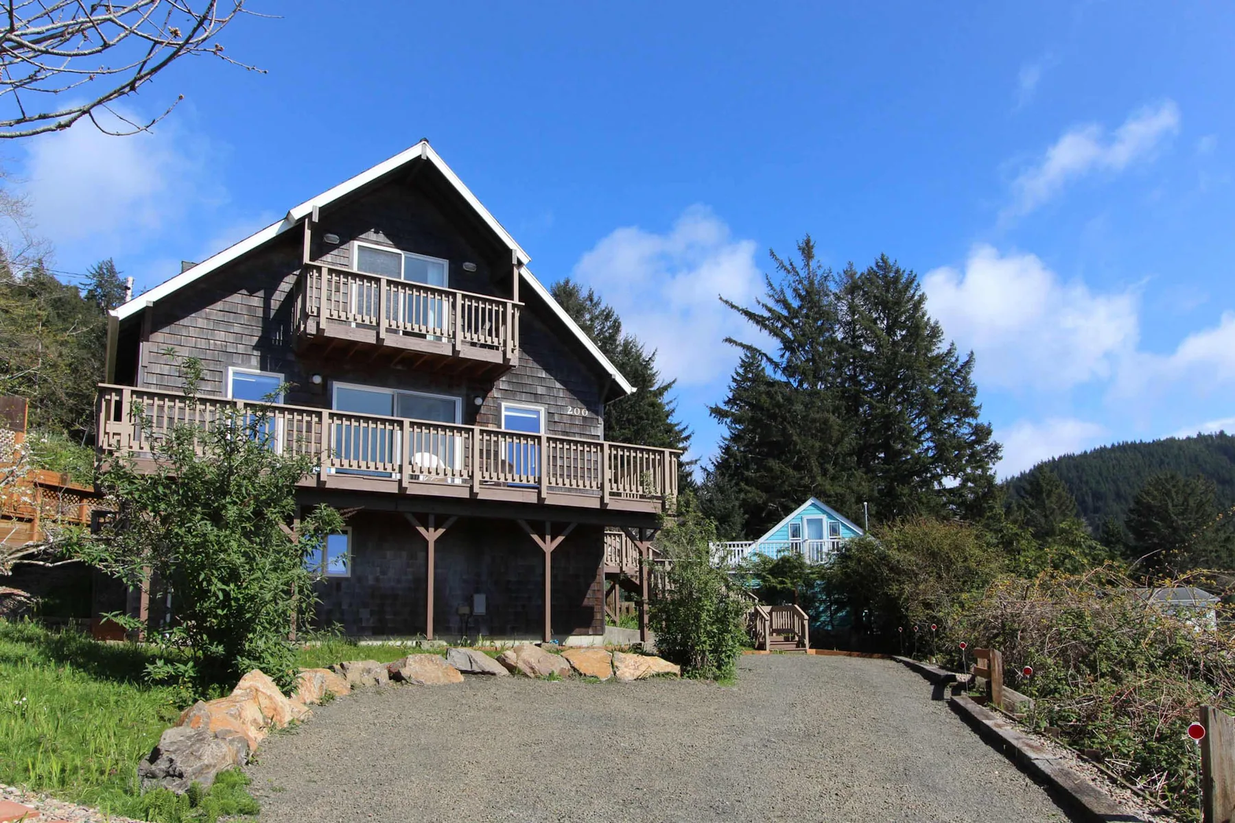 A multi-level house with wooden balconies stands beside a gravel driveway.