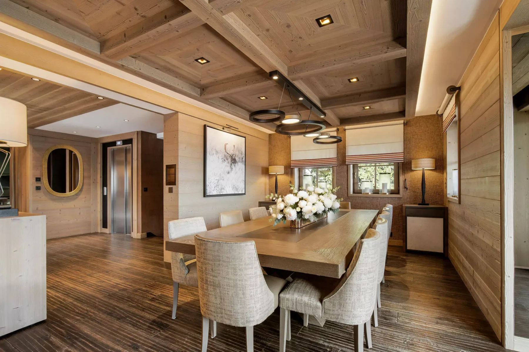 Comedor revestido de madera con una mesa larga, asientos tapizados y lámparas colgantes.