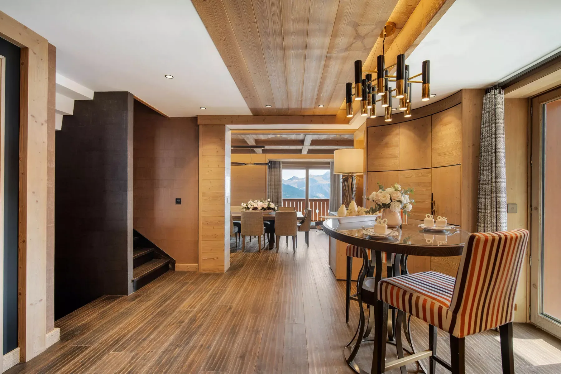 Un comedor revestido de madera con una mesa larga y asientos tapizados a rayas.