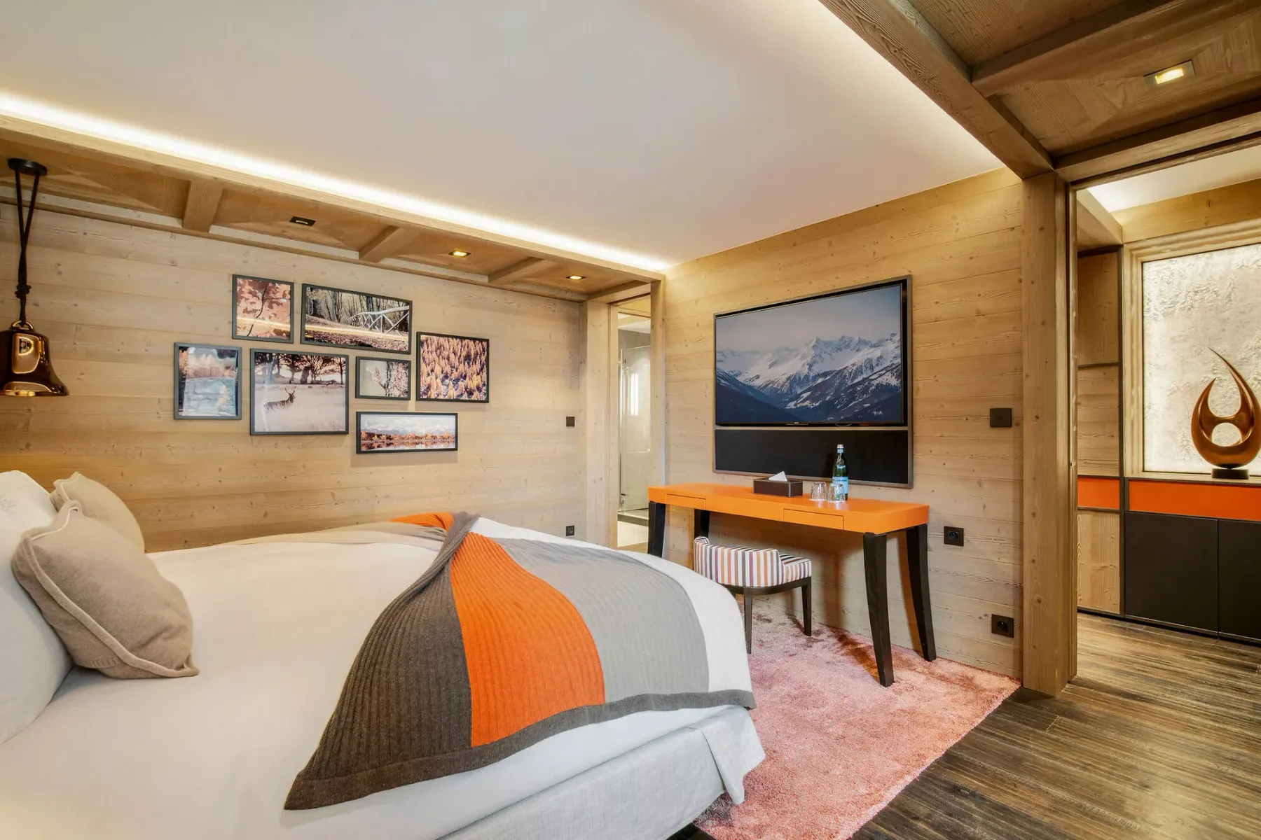 Un dormitorio con una cama, una manta colorida y un escritorio pequeño bajo una imagen de montañas.
