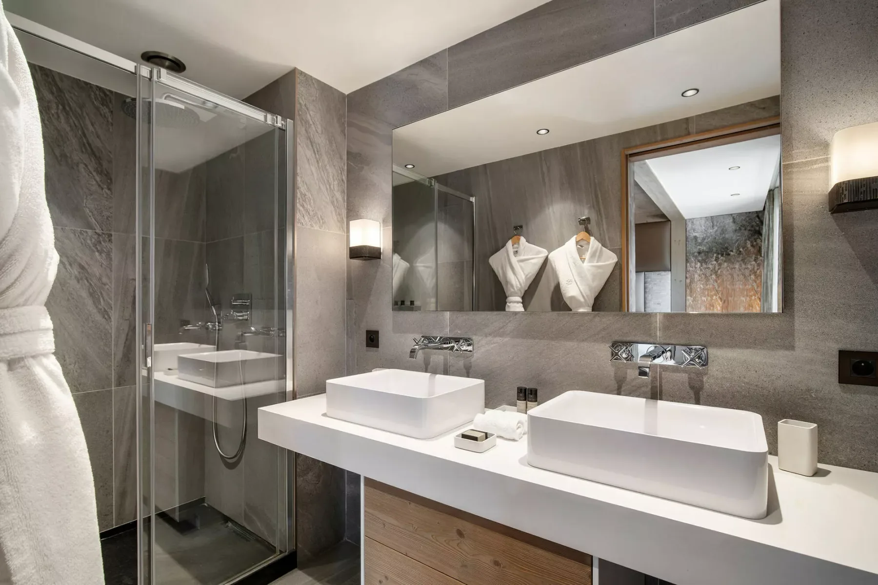 Un baño moderno con una ducha de vidrio y un amplio tocador con dos lavabos.