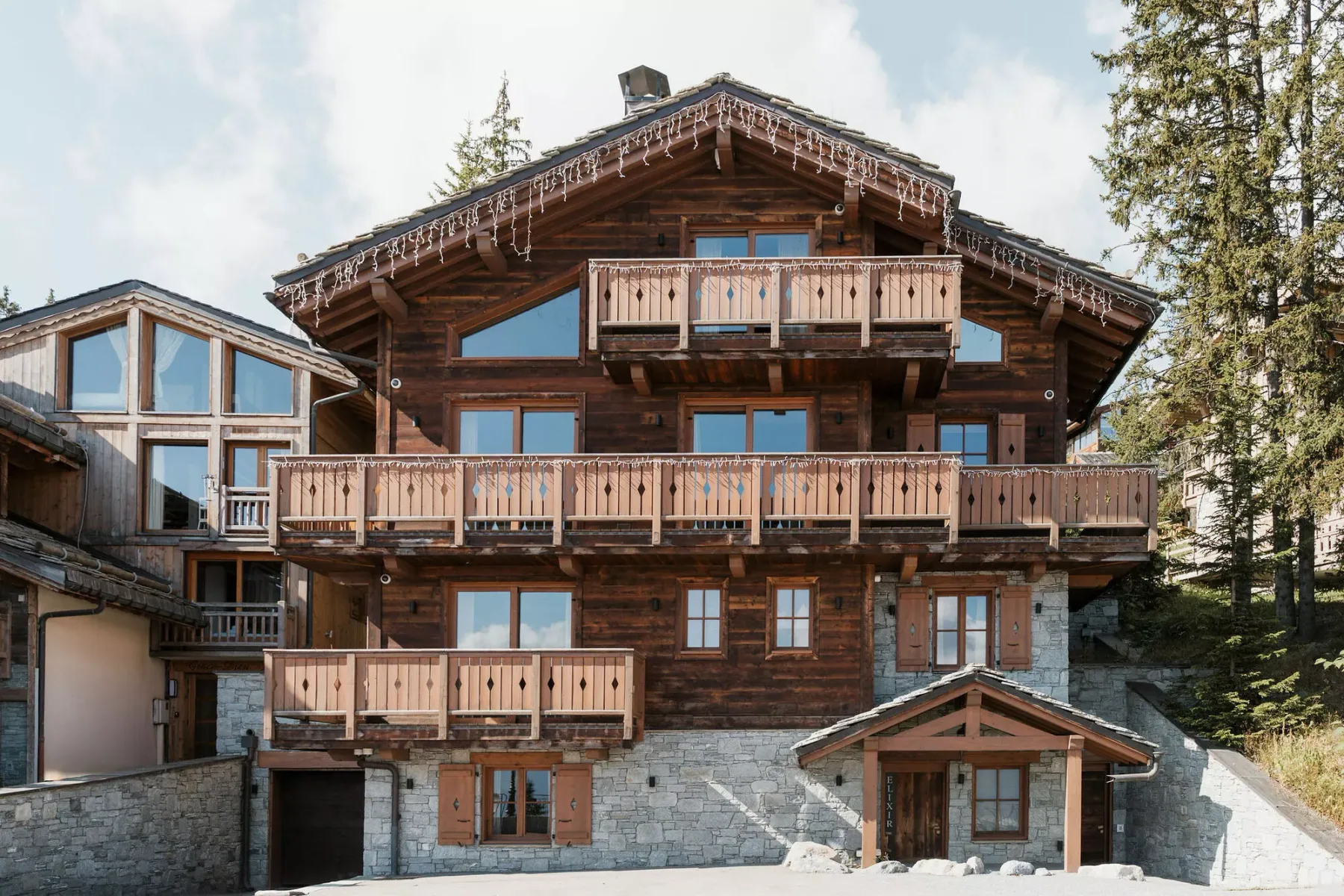 Una gran casa tipo chalet con balcones de madera se alza entre árboles.