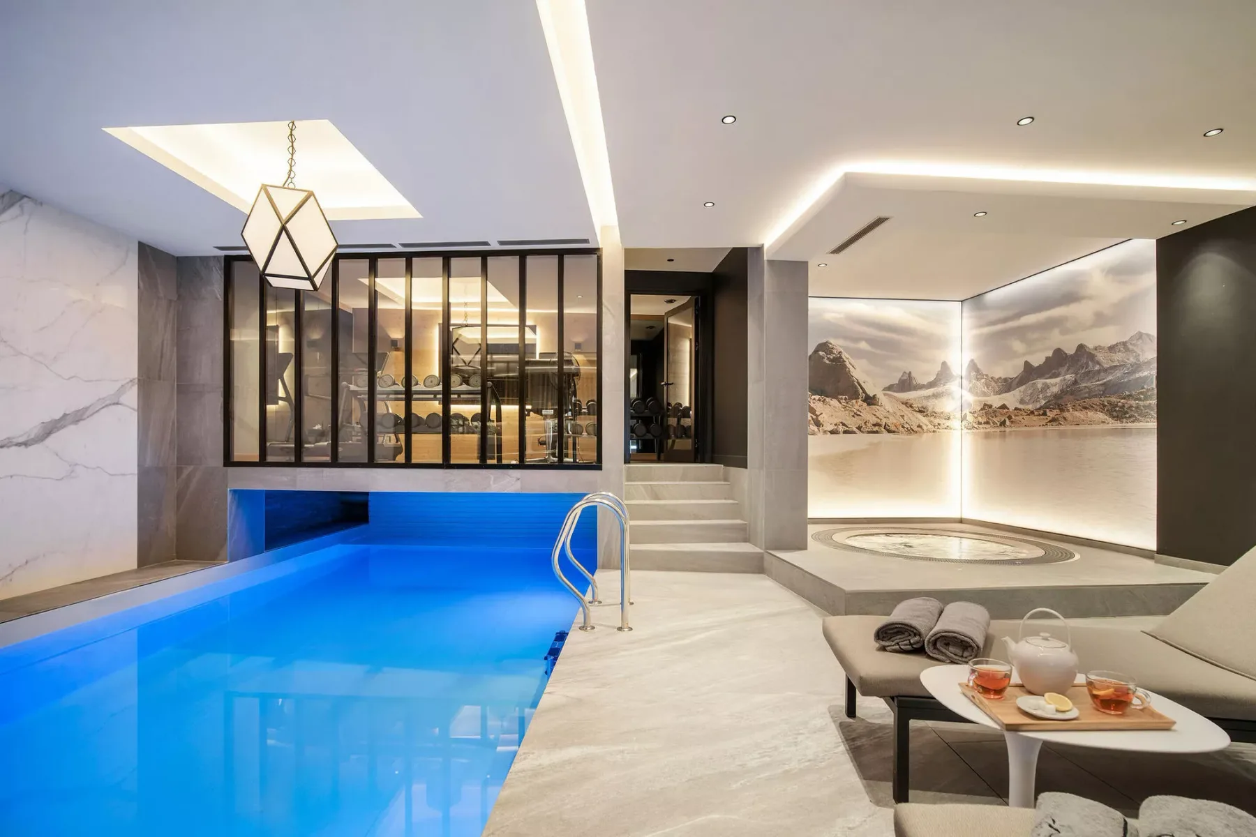 Una piscina cubierta moderna y zona de estar con puertas de vidrio y un mural de montañas.