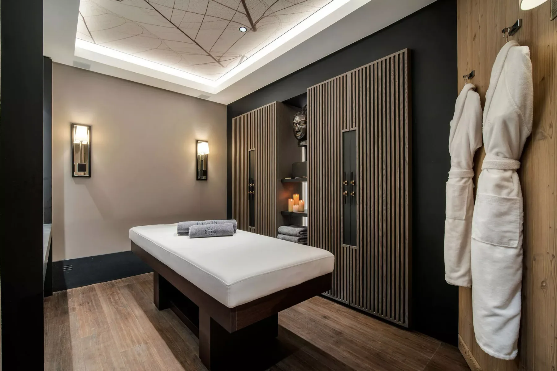 Sala de tratamiento de spa con una camilla de masaje y batas colgadas en la pared.