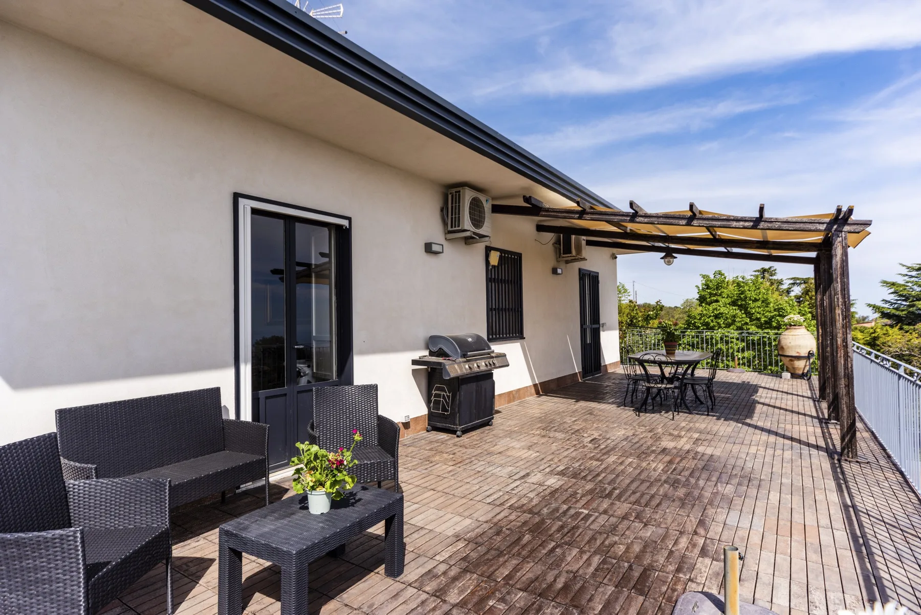 Una amplia terraza exterior junto a un edificio blanco, con asientos y una mesa de comedor.