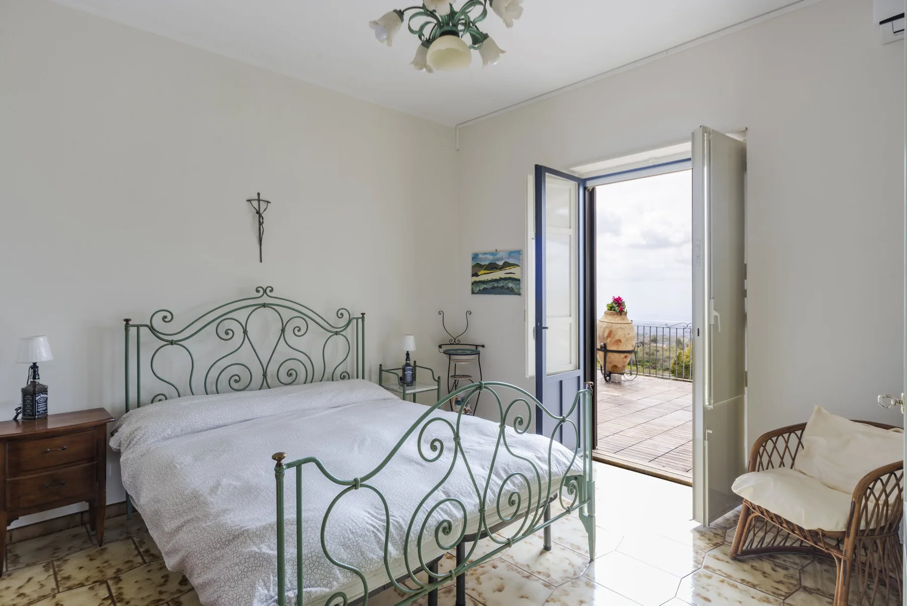 A bedroom with a metal bed and open doors leading to a balcony.