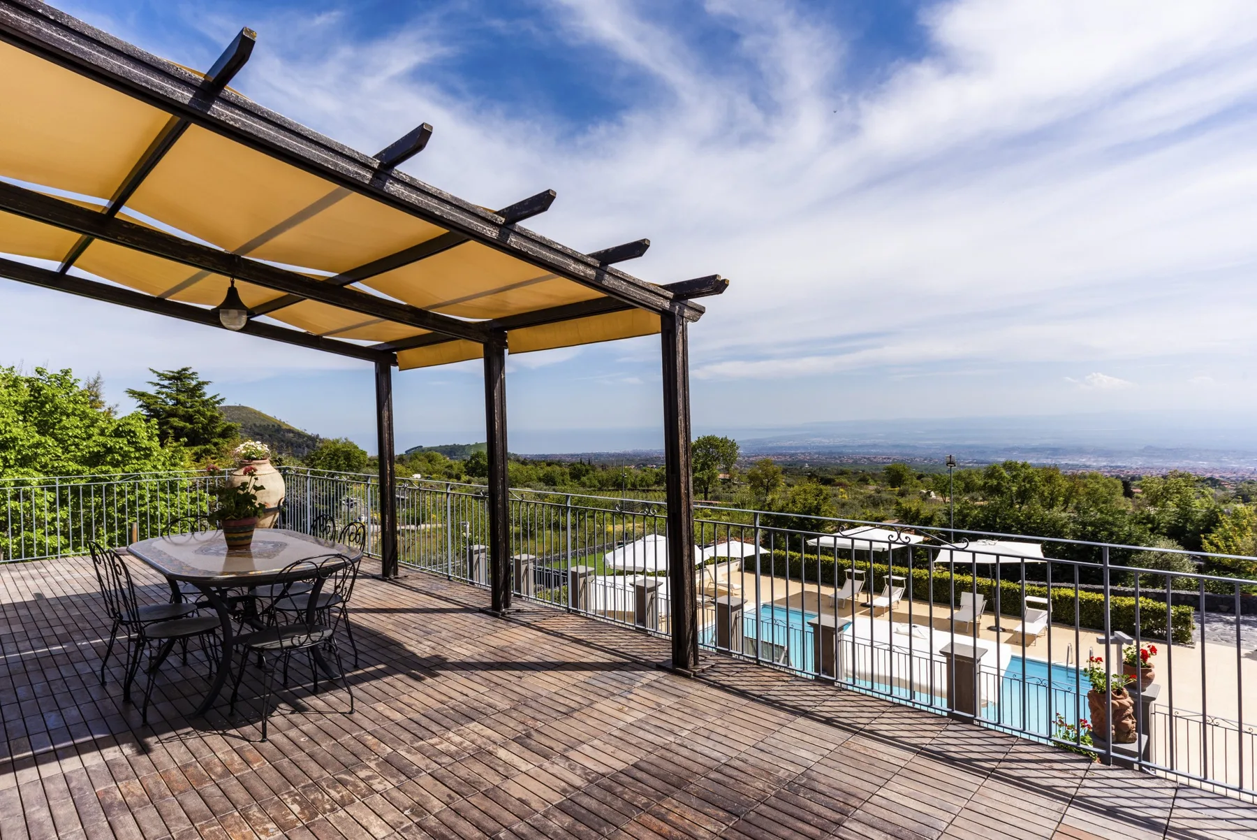 Una terraza exterior bajo un toldo mira hacia una piscina y un paisaje lejano.